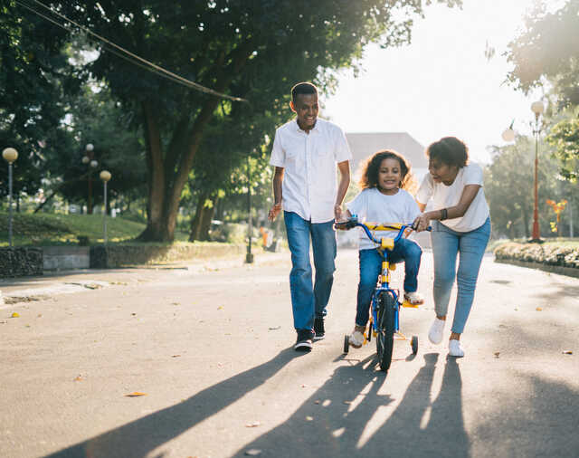 mother and father helping a daughter ride a bike