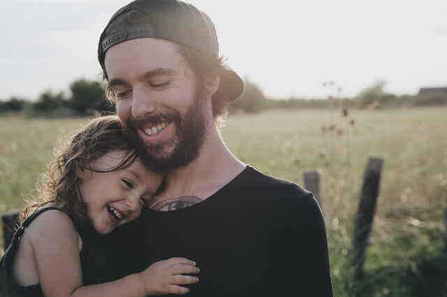 father snuggling daughter in a field